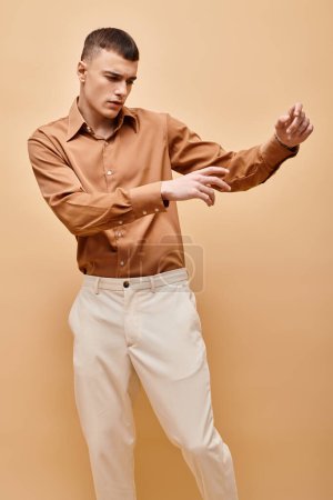 Foto de Portrait of stylish handsome man in beige shirt moving hands on peachy beige background - Imagen libre de derechos