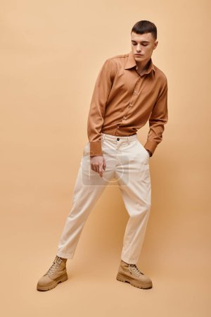 Imagen completa del joven en camisa beige, pantalones y botas posando sobre fondo beige