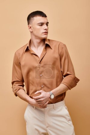 Portrait of stylish handsome man in beige shirt looking away on peachy beige background