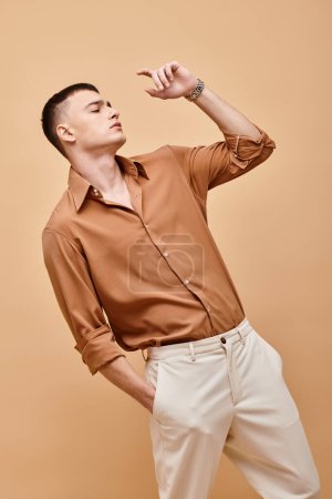 Modeaufnahme eines stilvollen Mannes im beigen Hemd, der mit der Hand in der Tasche vor beigem Hintergrund wegschaut