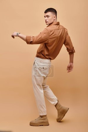 Photo for Full length photo of young man in beige shirt, pants and boots posing on beige background - Royalty Free Image