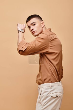 Fashion portrait of handsome man in beige shirt with hand near face on beige background