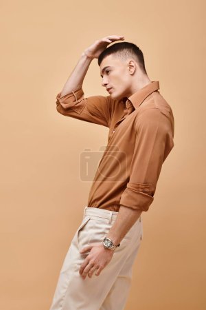 Foto de Side view photo of young man in beige stylish outfit and hand on hair posing on beige background - Imagen libre de derechos