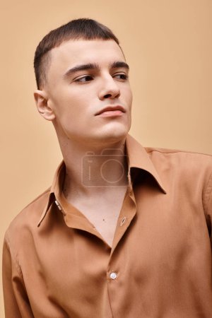 Modeporträt eines stilvollen jungen Mannes im beigen Hemd, der vor pfirsichbeigem Hintergrund wegschaut