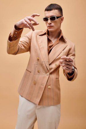 Portrait of stylish handsome man in beige jacket moving hands on peachy beige background