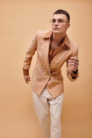 Foto de Retrato de hombre guapo en chaqueta beige y gafas posando sobre fondo beige melocotón - Imagen libre de derechos