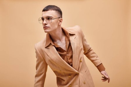 Foto de Hombre con estilo en sus años 20 posando en chaqueta beige con estilo y gafas sobre fondo beige melocotón - Imagen libre de derechos