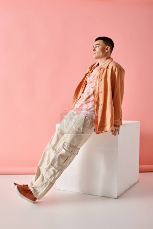 Photo for Fashion shot of fashionable man in beige shirt, pants and boots on white cube on pink background - Royalty Free Image