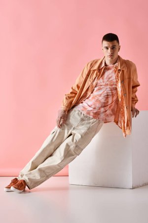 Foto de Full length image of stylish man in beige shirt, pants and boots on white cube on pink background - Imagen libre de derechos