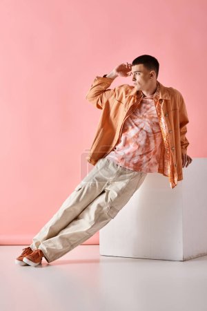 Photo for Fashion image of stylish man in beige shirt, pants and boots on white cube on pink backdrop - Royalty Free Image