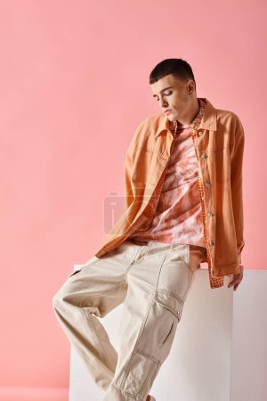 Photo for Full length of stylish man in beige shirt and trendy male pants on white cube on pink background - Royalty Free Image