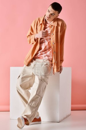 Foto de Fashion image of stylish man in beige shirt, pants and boots on white cube on pink backdrop - Imagen libre de derechos