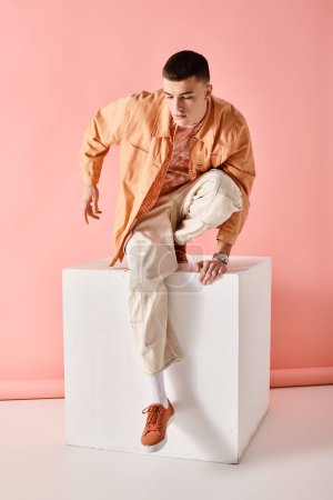 Foto de Hombre guapo en traje beige mirando hacia abajo y posando sobre cubo blanco sobre fondo rosa - Imagen libre de derechos