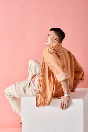 Photo for Side view image of stylish man in beige shirt, pants and boots on white cube on pink backdrop - Royalty Free Image