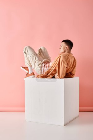 Photo for Side view photo of man in peach color outfit lying on white cube on pink background - Royalty Free Image