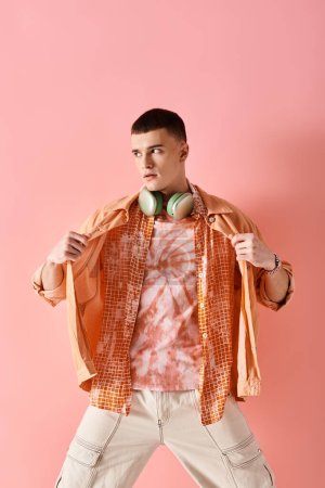 Téléchargez les photos : Image de mode de l'homme élégant en couches chemises avec écouteurs sans fil posant sur fond rose - en image libre de droit