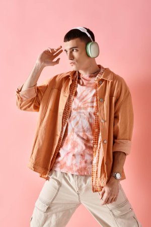 Young man in layered shirts with wireless headphones listening to music posing on pink backdrop