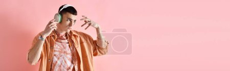 Retrato del hombre en traje de capas con auriculares inalámbricos bailando con música sobre fondo rosa, pancarta