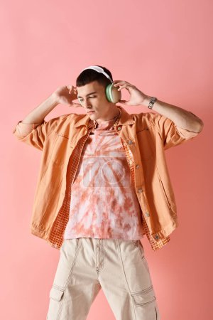Stylish man in layered outfit with wireless headphones dancing to music on pink background