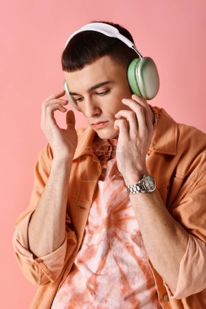 Téléchargez les photos : Beau homme avec écouteurs sans fil écoutant de la musique sur fond rose regardant vers le bas - en image libre de droit