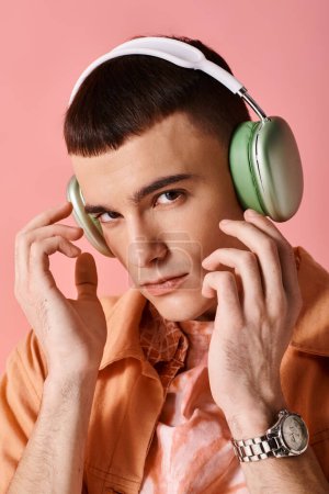 Téléchargez les photos : Handsome man with wireless headphones listening to music on pink background looking at camera - en image libre de droit