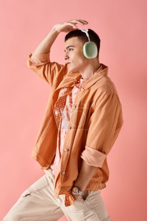 Téléchargez les photos : Vue latérale de l'homme élégant portant des écouteurs sans fil dansant sur la musique sur fond rose - en image libre de droit