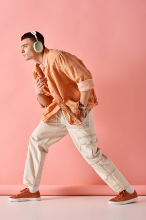 Téléchargez les photos : Photo pleine longueur de l'homme portant des écouteurs sans fil dansant sur la musique sur fond rose - en image libre de droit