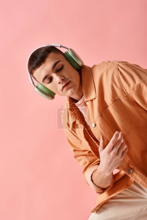 Téléchargez les photos : Beau homme avec écouteurs sans fil écoutant de la musique sur fond rose regardant vers le bas - en image libre de droit