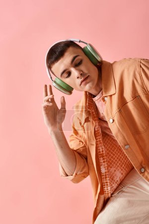 Téléchargez les photos : Homme à la mode en tenue à couches avec écouteurs sans fil écoutant de la musique sur fond rose - en image libre de droit