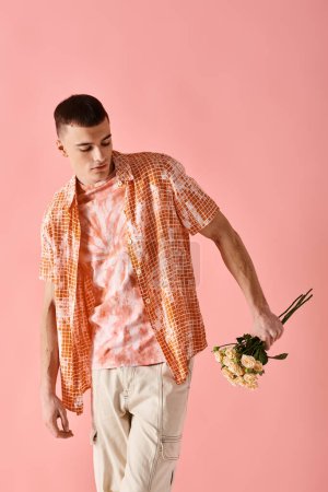 Portrait de mode d'homme à la mode en tenue superposée tenant des fleurs sur fond rose
