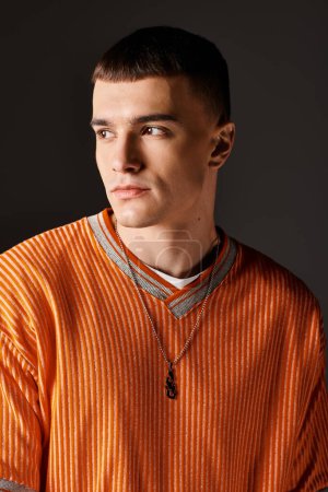 Foto de Retrato de moda de hombre guapo con estilo en jersey naranja mirando hacia otro lado sobre fondo gris - Imagen libre de derechos
