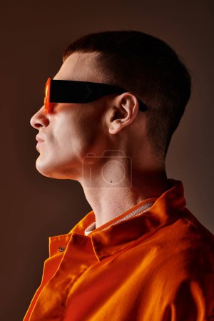 Foto de Imagen vista lateral del hombre con estilo en camisa naranja y gafas de sol sobre fondo marrón - Imagen libre de derechos