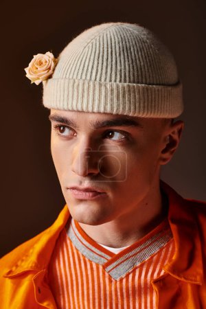 Téléchargez les photos : Portrait d'un bel homme en tenue orange portant un bonnet beige avec des fleurs sur fond marron - en image libre de droit