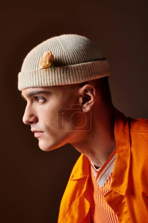 Photo for Side view of stylish man in orange outfit wearing beige beanie with flower in studio - Royalty Free Image