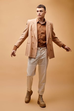 Ganzes Porträt eines modischen Mannes in beiger Jacke, Hemd, Hose und Stiefeln auf beigem Hintergrund