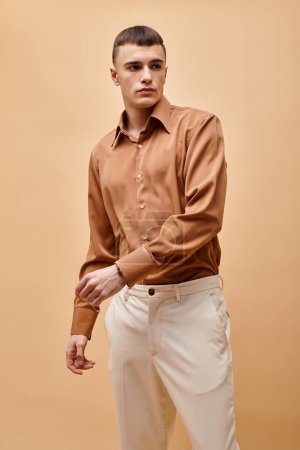 Portrait of stylish handsome man in beige shirt moving hands on peachy beige background