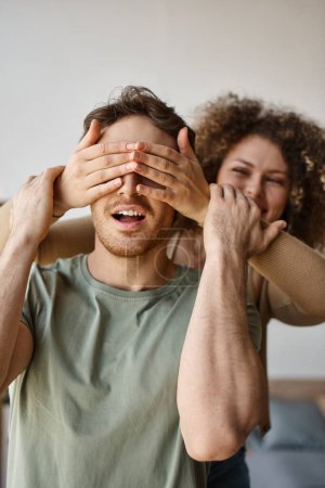Adoring couple, curly young woman covering eyes of brunette man, sharing a loving moment with smiles