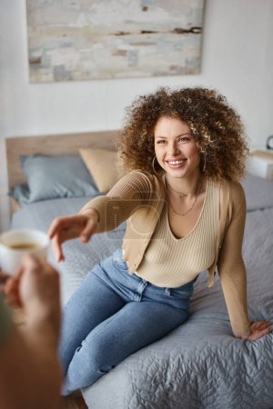Mujer rizada mujer sonriente tomando una taza de café de mano novios, cuidando y disfrutando del tiempo en casa