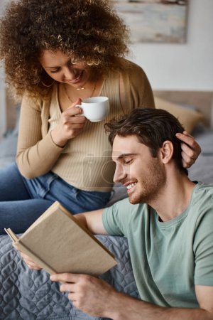 lockige junge Frau und brünetter Mann unterhalten sich lebhaft bei Kaffee, Buch in den Händen