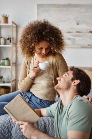 Warmer Morgendialog bei Kaffee, lockige junge Frau und brünetter Mann teilen einen gemütlichen Moment im Bett