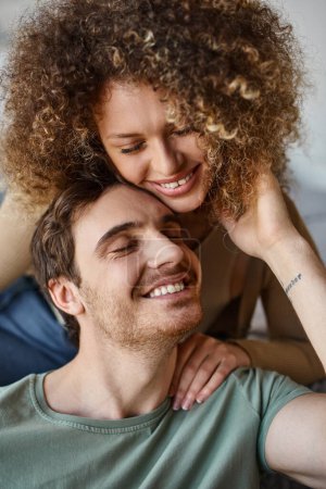 Loving couple, curly young woman and brunette man, hugging tightly with happy smiles
