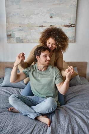 Téléchargez les photos : Jeune femme bouclée et homme brune profiter d'un câlin affectueux dans leur matin paisible dans leur lit confortable - en image libre de droit
