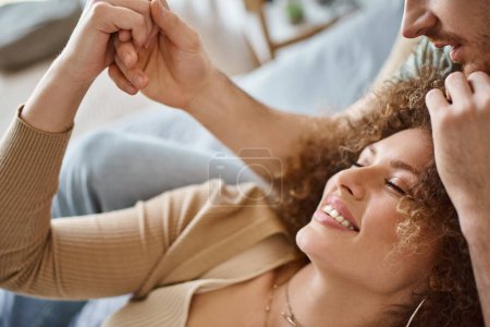 Téléchargez les photos : Gros plan de frisé jeune femme heureuse couché avec son petit ami souriant et tenant la main - en image libre de droit