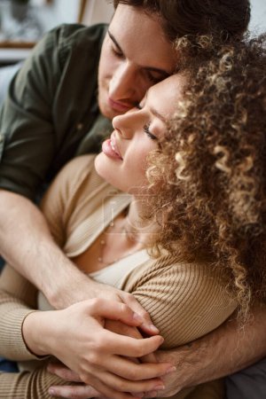 Closeup photo of curly young woman and brunette man sharing a heartfelt hug in bedroom