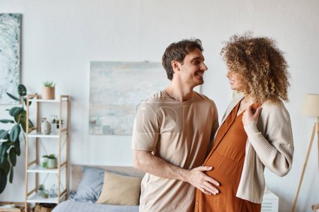 Couple in love in their bedroom, embracing and smiling to each other as they wait for baby