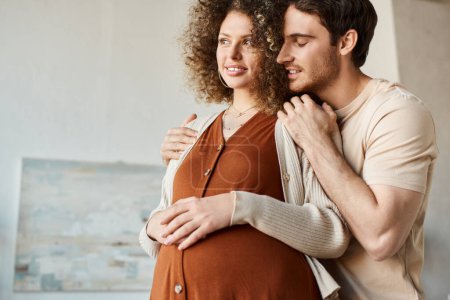 Loving young man and pregnant woman holding hands on belly, feeling inspired waiting for baby