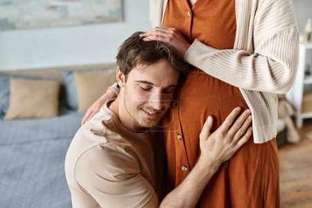 Cropped image of husband listening to baby in pregnant wife belly, hugging parents