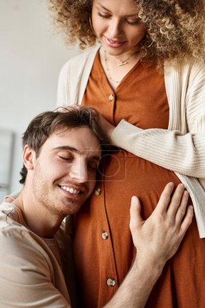 Emotional moment of happy man listening to baby hugging tummy of wife, touching her belly