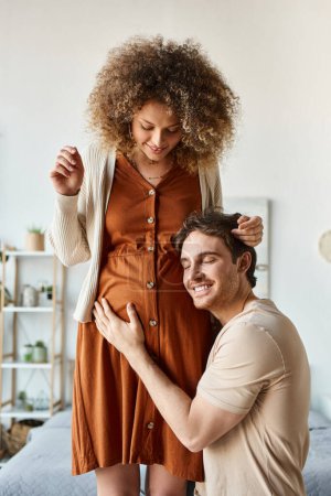 Lovely couple waiting for baby. Handsome smiling happy man listening to baby hugging belly of wife