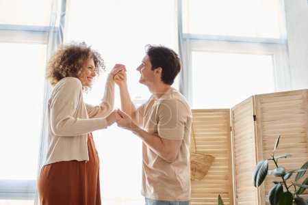 Couple expecting child spending time together at home dancing holding hands with smile